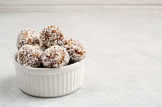 Energy balls of dates, nuts, oats, sprinkled with coconut powder closeup in a white plate on a white background background with copy space