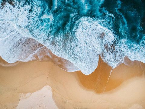 drone aerial view of ocean surf crashing on empty beach blue