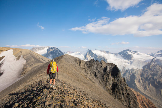 Rear view of backpacker hiking on rocky summit ridge.