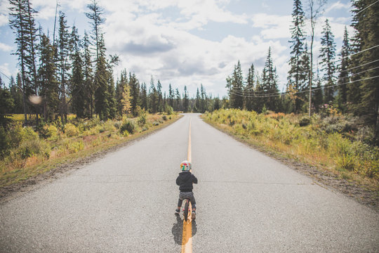 Rear view of toddler boy biking on yellow line on road.