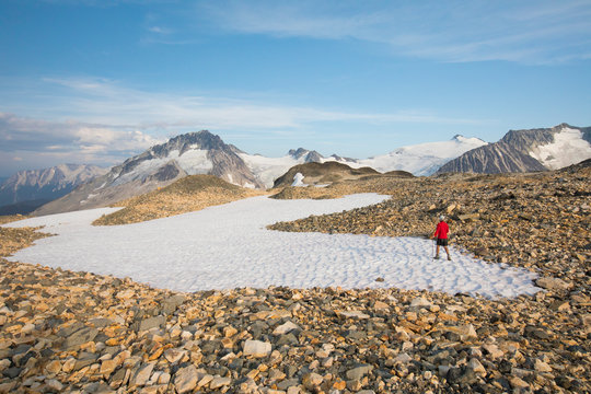 hiker crossing snow patch in rocky terrain.