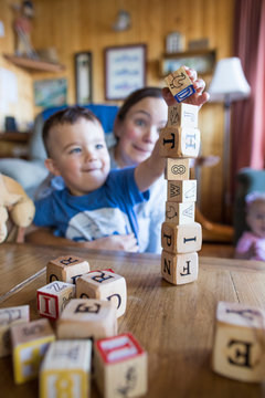 Mother worries as son places wooden block on tower.