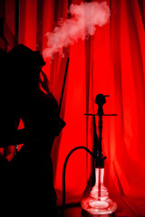 silhouette of a girl Smoking a hookah on a red background and exhales smoke