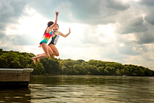 Two Young Girls in Swimsuits Jumping off a Dock into a Lake