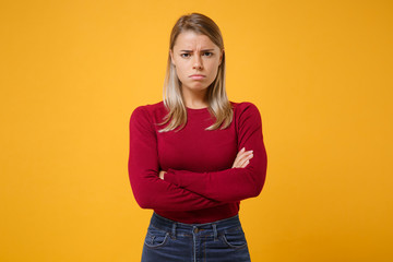 Displeased offended young blonde woman in casual clothes posing isolated on yellow orange background in studio. People sincere emotions lifestyle concept. Mock up copy space. Holding hands crossed.