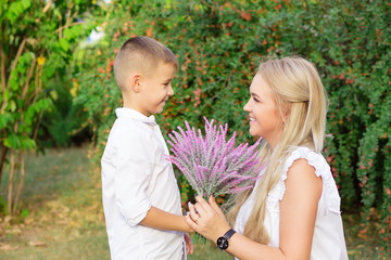 Happy mothers day. Son giving flowers to mom outside isolated green foliage background