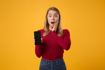 Shocked young blonde woman girl in casual clothes posing isolated on yellow orange background. People lifestyle concept. Mock up copy space Hold mobile phone with blank empty screen put hand on cheek.