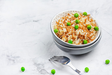 A pilaf of rice and fried noodles decorated with green peas. Turkish national side dish. Photograph on a light background with copy space.
