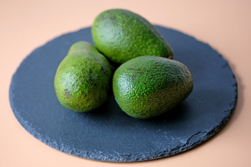 Three green avocados on a black slate plank. Fresh avocado on the table.
