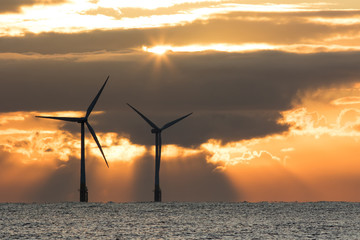 Dramatic sky. Solar and wind power. Offshore turbines at sunrise.