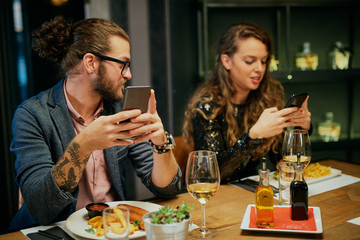 Bored couple sitting in restaurant for dinner and using smart phones.
