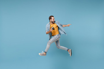 Fototapeta na wymiar Excited traveler tourist man in yellow clothes with photo camera isolated on blue background. Male passenger traveling abroad on weekend. Air flight journey concept. Jumping, point index finger aside.