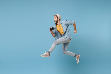 Fototapeta na wymiar Side view of excited traveler tourist man in yellow clothes with photo camera isolated on blue background. Male passenger traveling abroad on weekend. Air flight journey concept. Jumping like running.