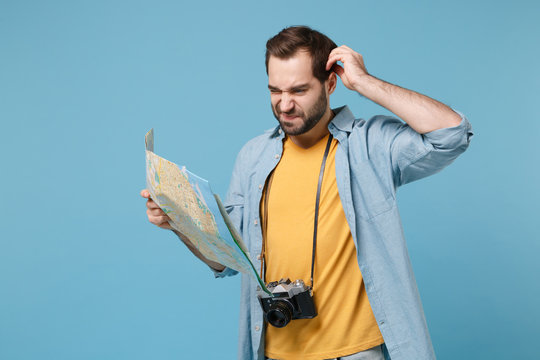 Confused traveler tourist man in summer yellow clothes with photo camera isolated on blue background. Passenger traveling abroad on weekends. Air flight journey concept Hold city map put hand on head.