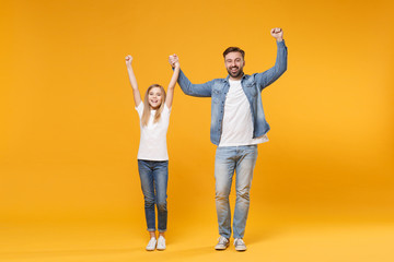 Happy bearded man in casual clothes with child baby girl. Father little kid daughter isolated on yellow background. Love family parenthood childhood concept. Rising holding hands doing winner gesture.