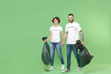 Cheerful two young friends couple in white volunteer t-shirt isolated on pastel green wall...