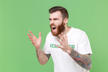 Angry young bearded man in volunteer t-shirt isolated on pastel green background. Voluntary free...