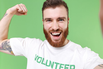 Close up of strong man in volunteer t-shirt isolated on green background. Voluntary free work...