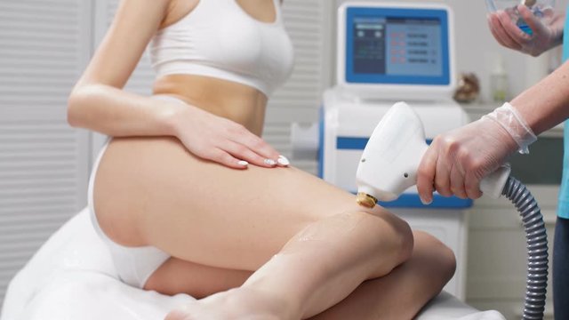 Close-up photo of young woman getting laser hair removal procedure on her legs in modern clinic. Cosmetology and spa, skin care concept.