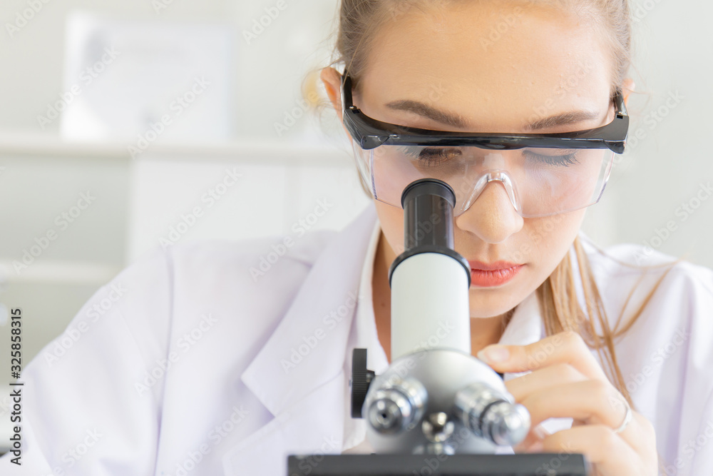 Poster Beautiful female scientists are looking at the microscopes in a science lab with various equipment in the laboratory.