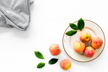 Summer lunch. Red peaches on white background with tablecloth and leaves top-down copy space