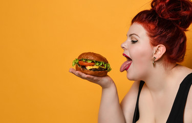 Happy size-plus overweight fat woman happy hold burger cheeseburger sandwich with beef on yellow