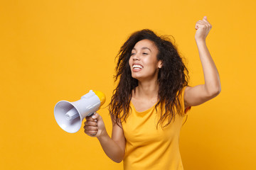 Joyful young african american woman girl in casual t-shirt posing isolated on yellow orange background in studio. People lifestyle concept. Mock up copy space. Hold megaphone, doing winner gesture.