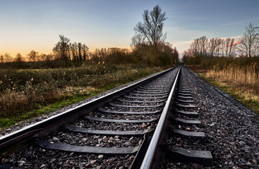 Fototapeta na wymiar Railway track in rural landscape with sunset sky