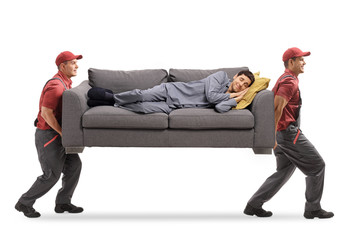 Two movers carrying a couch and a man in pajamas sleeping on it