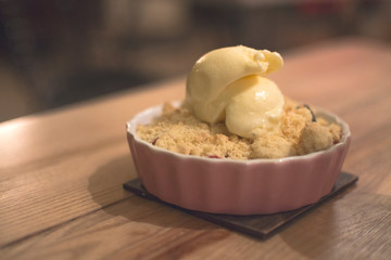 Apple crumble pie with vanilla ice creamin pink ceramic baking dish on wooden table.Tasty sweet dessert, rustic cake. Restaurant service. Healthy homemade food, crispy pastry, close up. Copy space.