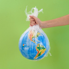 Earth in polyethylene plastic, in hand on white background. Concept pollution of environment with plastic waste. Stop plastic pollution