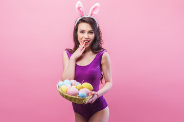 Attractive hot young woman wearing bodysuit and bunny ears posing on pink background.