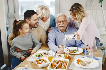 Happy extended family having fun while taking selfie with smart phone in dining room.