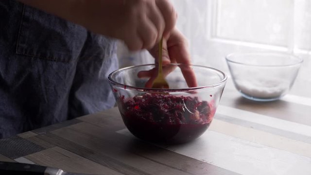 beautiful mature woman in red sweater and gray economic apron prepares salad of boiled beets, garlic and mayonnaise. girl rubs the beets, squeezes garlic and season with mayonnaise