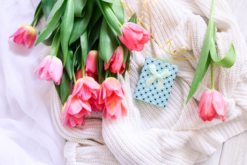 Gift box and bouquet of pink tulips on bed