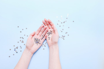 Hands with sparkling stars decorations on blue background. Stylish atmospheric image. Happy birthday concept. Holiday decor. Magic in hands. Christmas