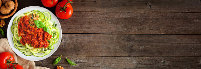 Zucchini pasta topped with meatless walnut cauliflower bolognese. Above view table scene on a rustic wood banner background. Healthy eating, plant-based meat substitute concept.
