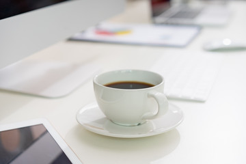 A cup of coffee and office supplies on the white desk