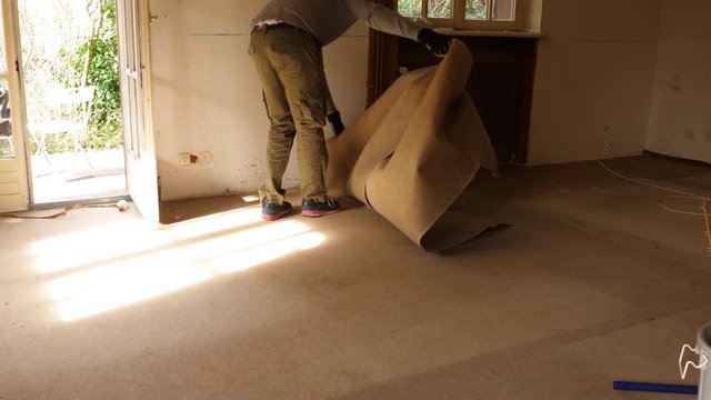 Powerful adult male worker wearing protective mask removing old dusty carpet in the empty house room during general renovation reconstruction