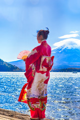Asian Woman In Traditional Japanese Kimono And Fan Posing at Fuji Mountain at Kawaguchiko Lake in Japan.