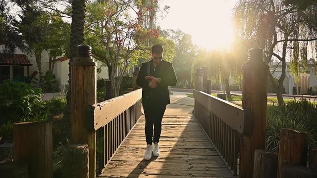 Dreamy hot guy in suit walks on backlit bridge looking at watch