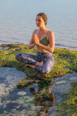Young woman, meditating, practicing yoga and pranayama at the beach. Sunset yoga practice. Hands in...