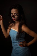 Portrait of Asian/Japanese/Korean/Indian brunette young girl in blue bath towel  and spectacles smoking cigarette in black studio copy space background. Indian lifestyle and fashion photography