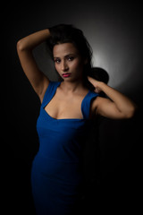 Fototapeta na wymiar Fashion portrait of an young and attractive Indian Bengali brunette girl with blue western dress in front of a black studio background. Indian fashion portrait and lifestyle.
