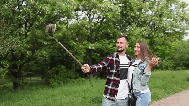 Happy young couple makes a joint selfie photo on the background of the green trees in the park.