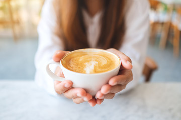 Closeup image of a woman holding and showing a cup of hot coffee