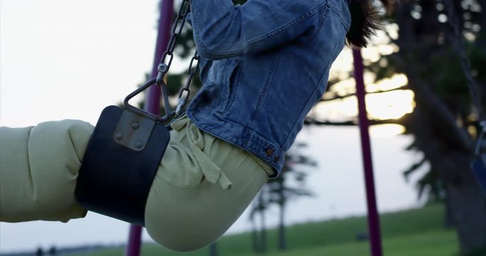 Woman in jean jacket swings on swing set during cool sunset - tracking shot
