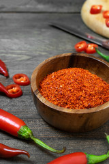 Cayenne in small bowl with chili on wooden table.