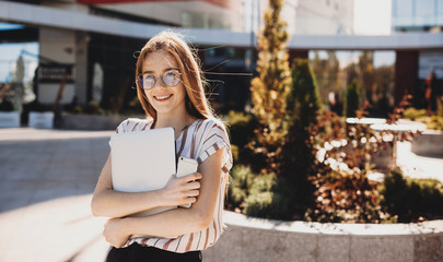 Fototapeta premium Gorgeous ginger girl with freckles is looking at camera and smiling while holding a laptop and a phone