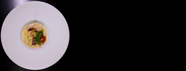 Spaghetti carbonara. Served with cheese, grilled bacon, cherry tomato, mint on a white plate.Isolated on a black background.Panorama for banners.Copy spase